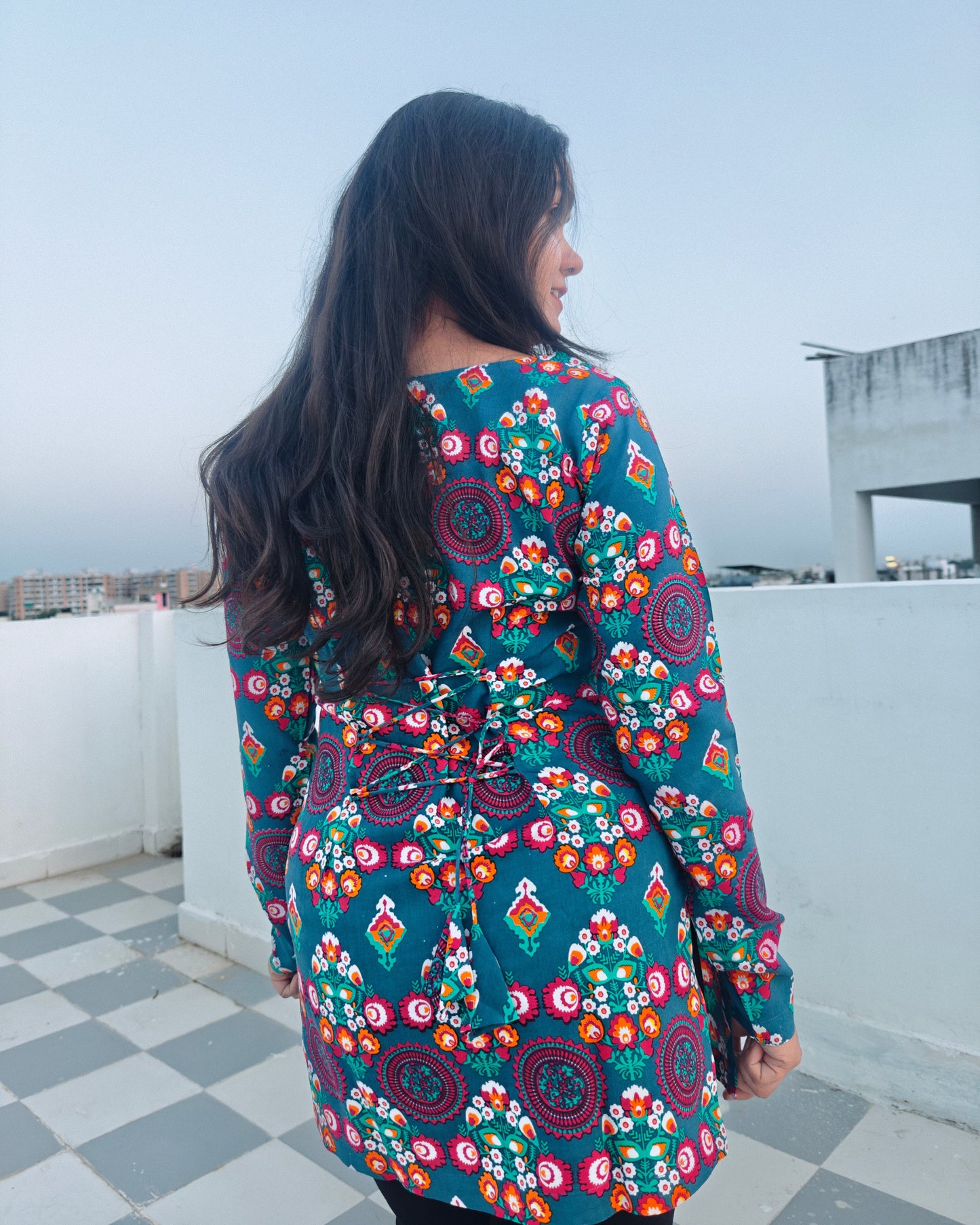 Person wearing a colorful floral dress on a rooftop with a cityscape background