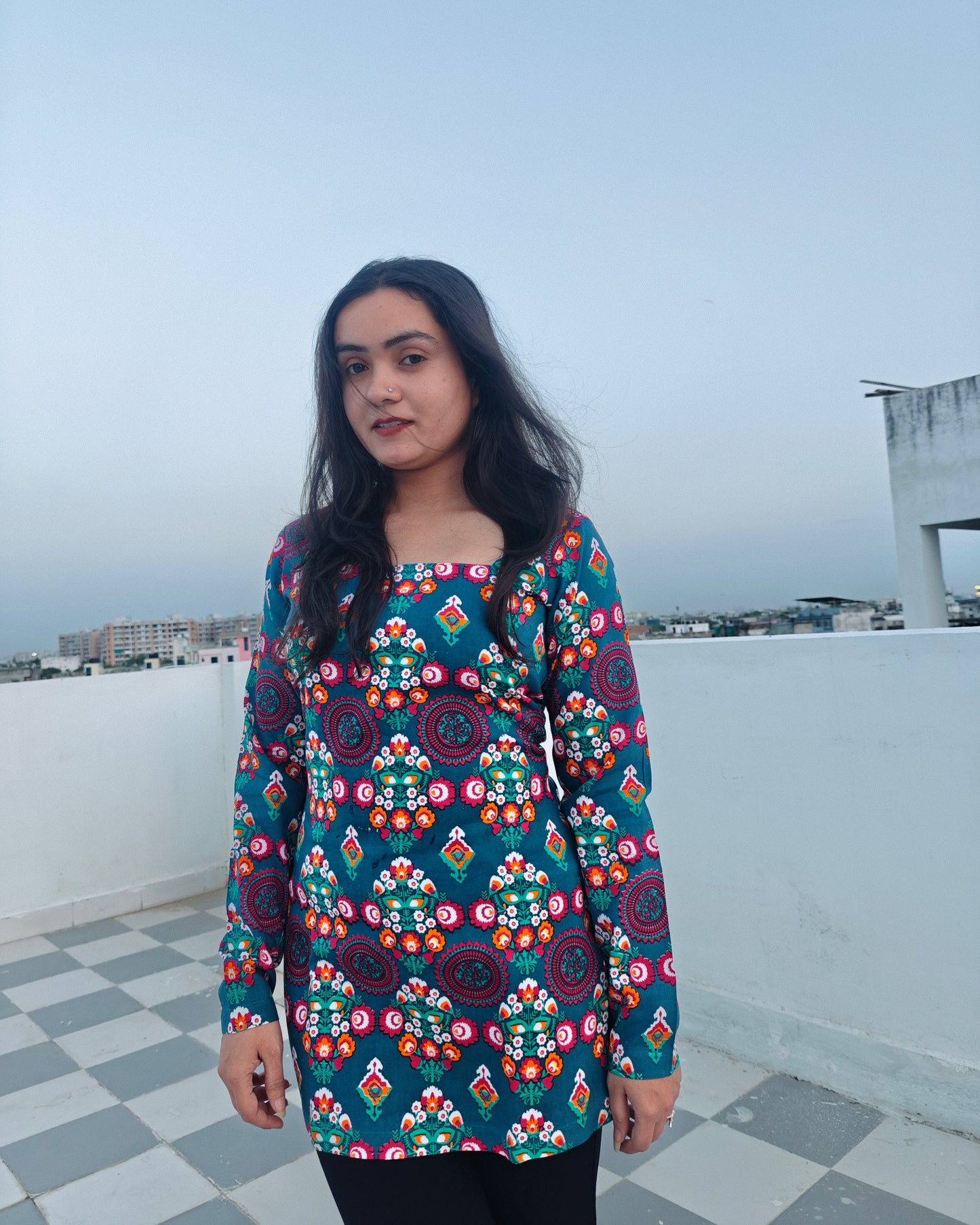 Woman wearing a colorful patterned dress on a rooftop with a cityscape in the background