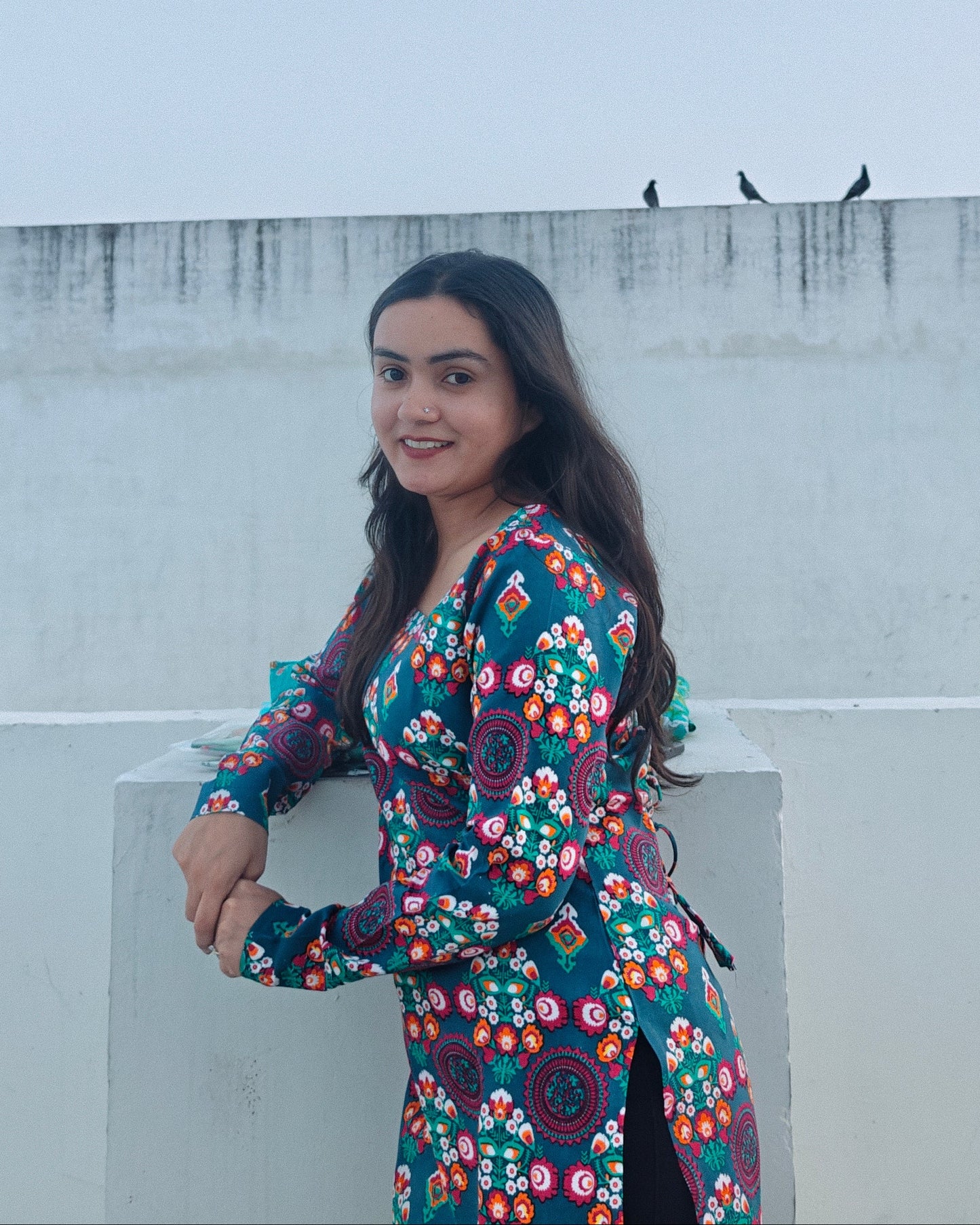 Woman in a floral dress standing on a rooftop with a plain background