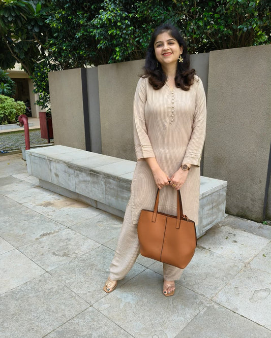 Woman in a beige outfit holding a brown bag outdoors.