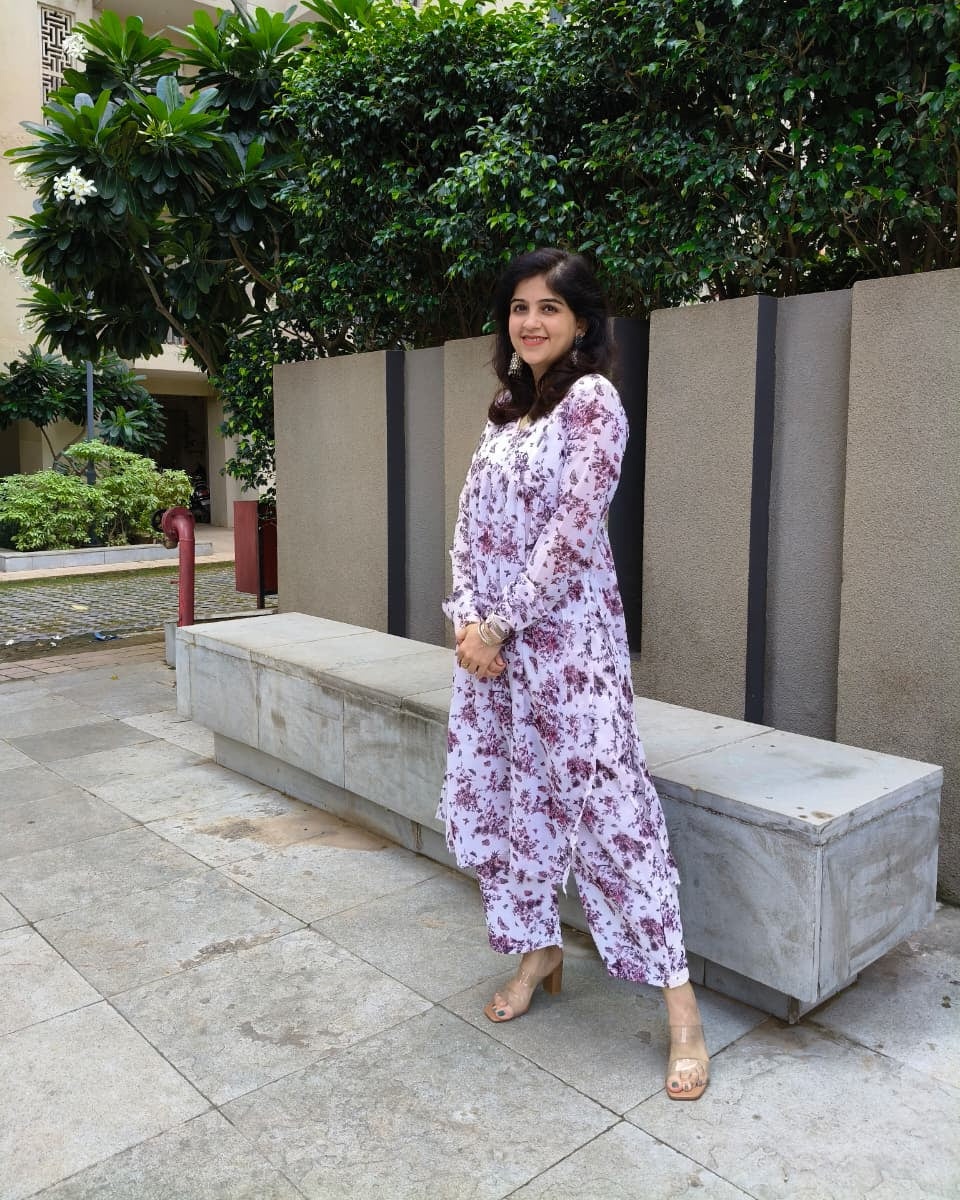 Woman in a floral dress standing outdoors near a concrete bench with greenery in the background