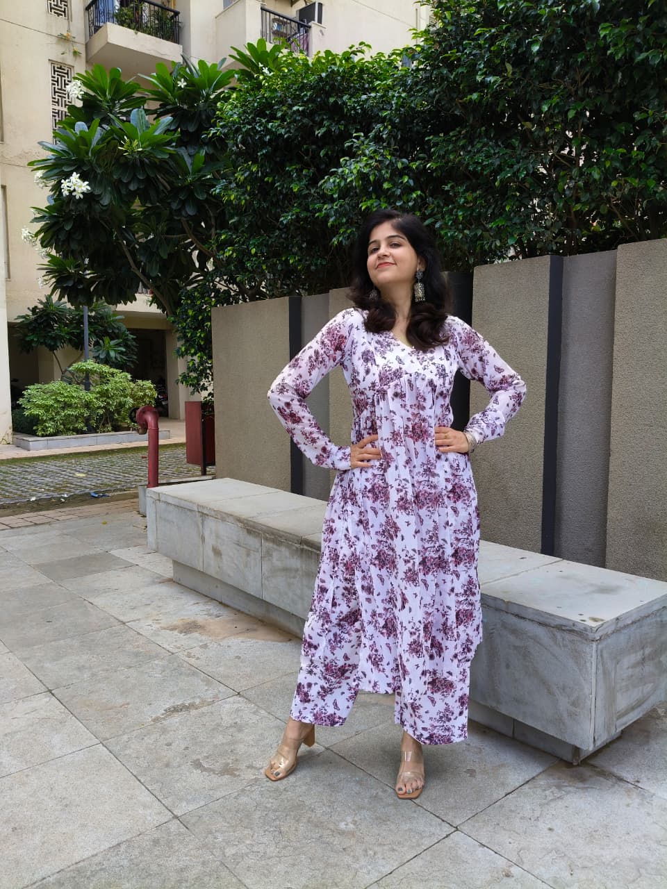 Woman in a floral dress standing outdoors with trees and buildings in the background
