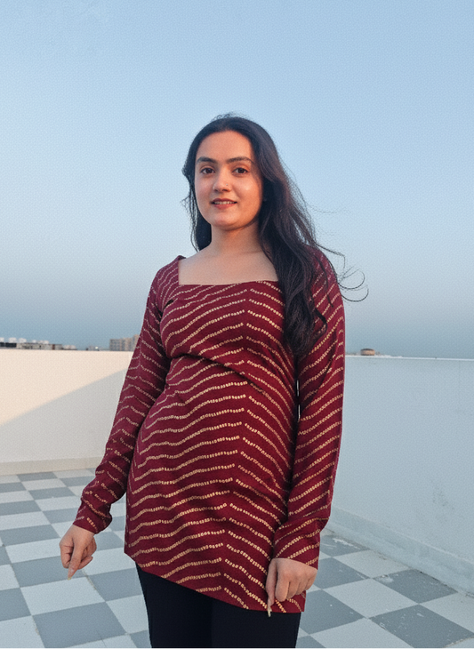 Woman wearing a red patterned top on a rooftop with a clear sky.
