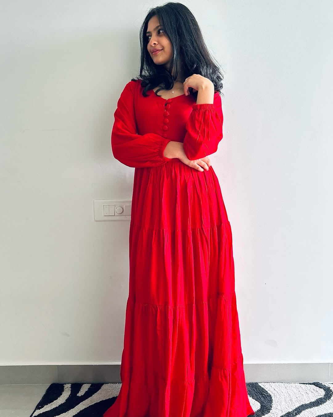 Woman wearing a red dress standing against a white wall.