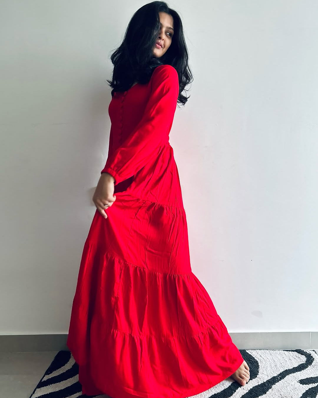 Woman wearing a red dress standing on a striped rug against a white wall