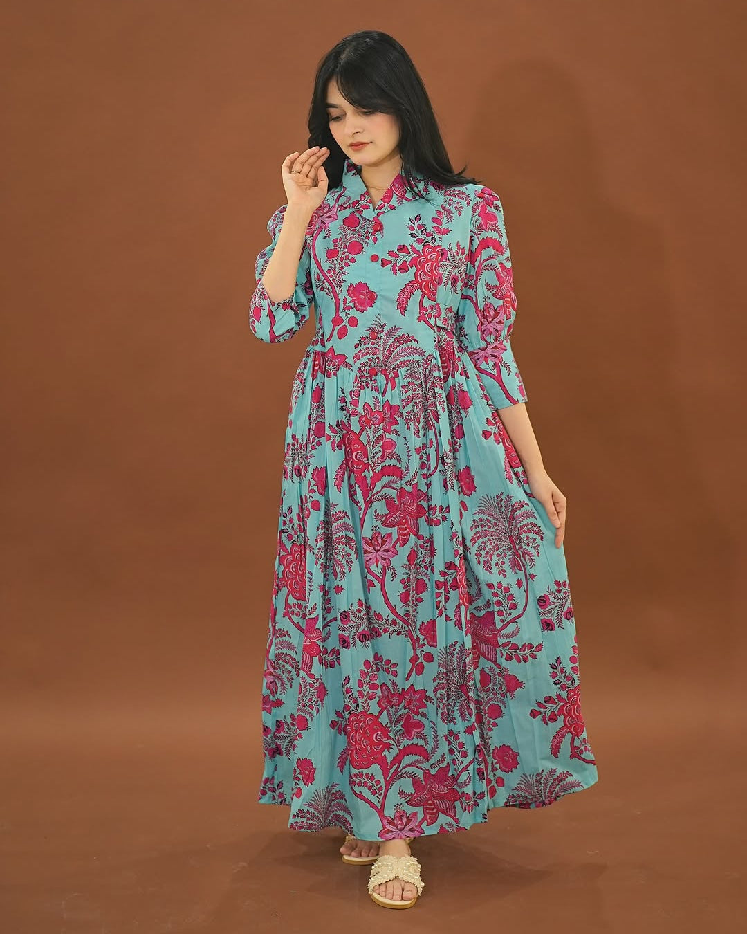 Woman wearing a turquoise dress with pink floral pattern against a brown background