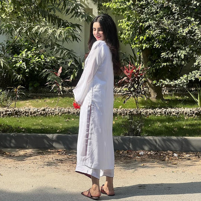 Woman in a white outfit standing outdoors with greenery in the background