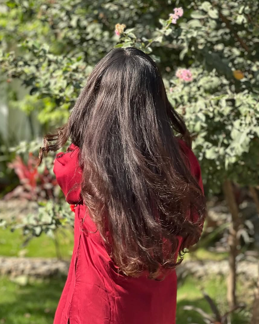 Person with long dark hair wearing a red outfit standing in a garden.