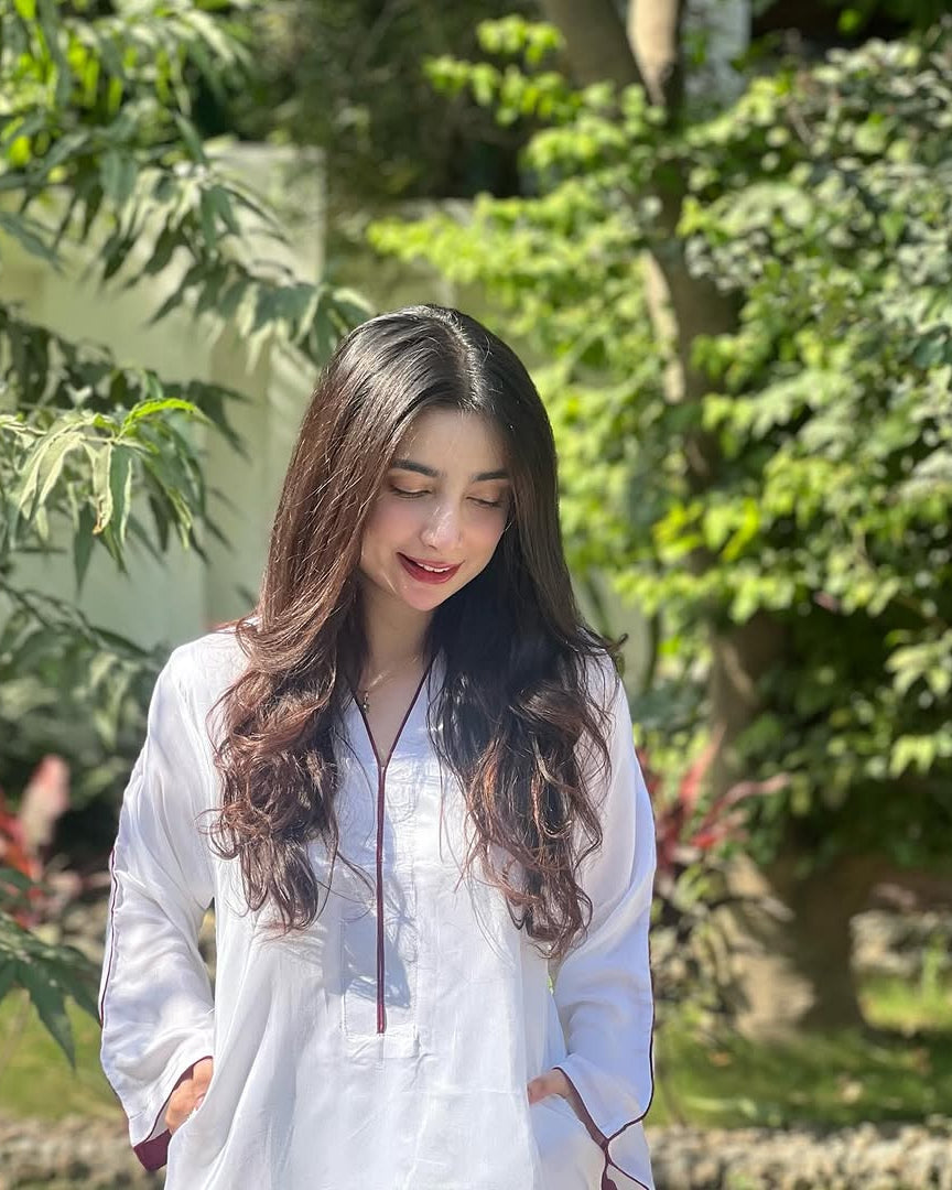 Woman in a white outfit standing among green foliage