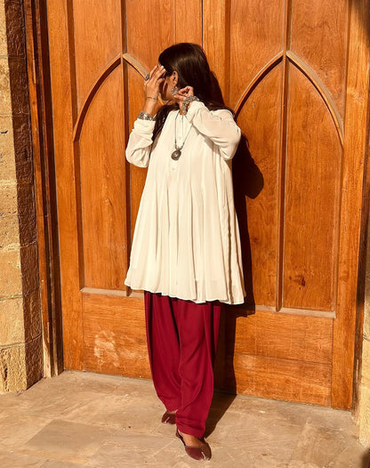 Person wearing a white top and red pants standing in front of a wooden door.