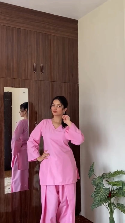 Woman in a pink outfit standing in front of a wooden wardrobe with a mirror.