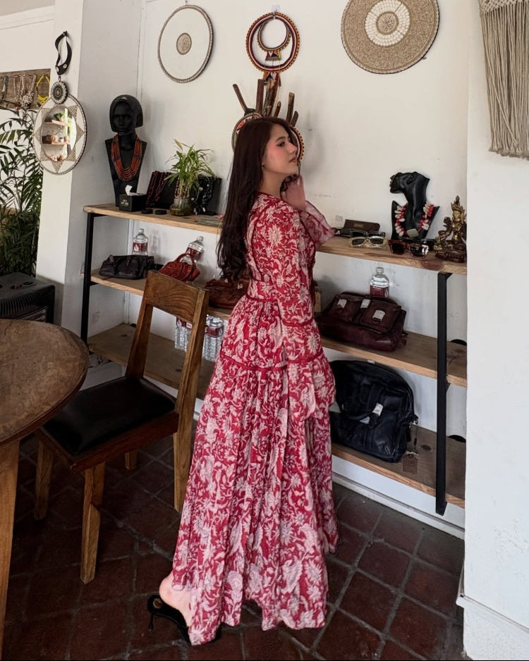 Woman in a red and white patterned dress standing in a room with shelves and decor.