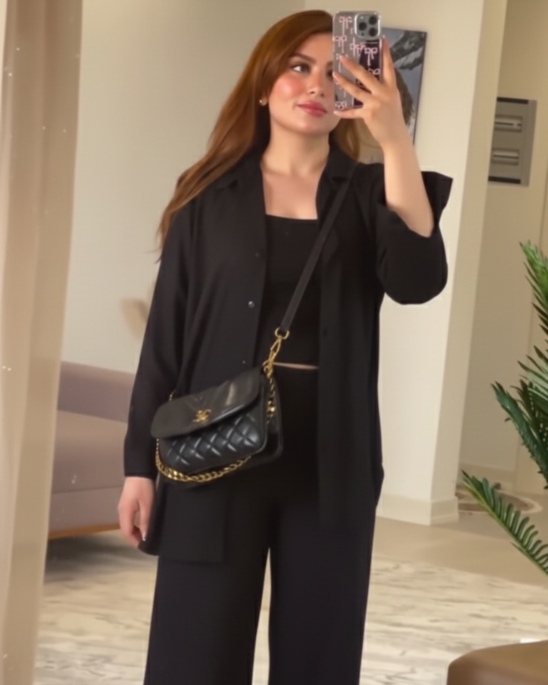 Person taking a mirror selfie wearing a black outfit with a black handbag indoors.