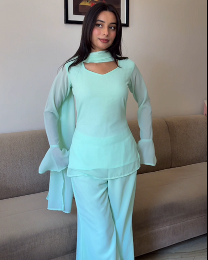 Woman in a light green outfit standing in a room with a couch and decorative wall art.