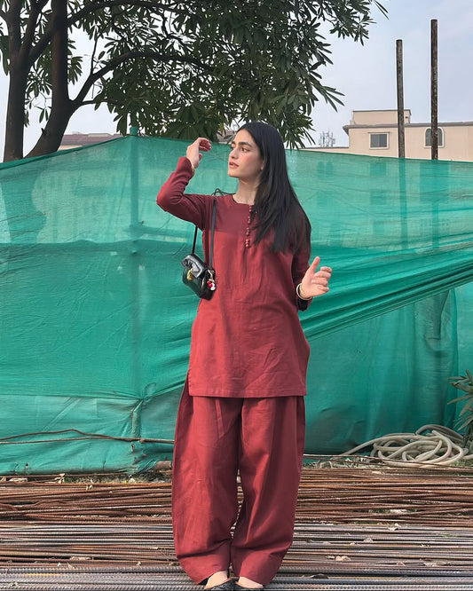 Person wearing a maroon Farshi salwar standing outdoors with green tarp and trees in the background
