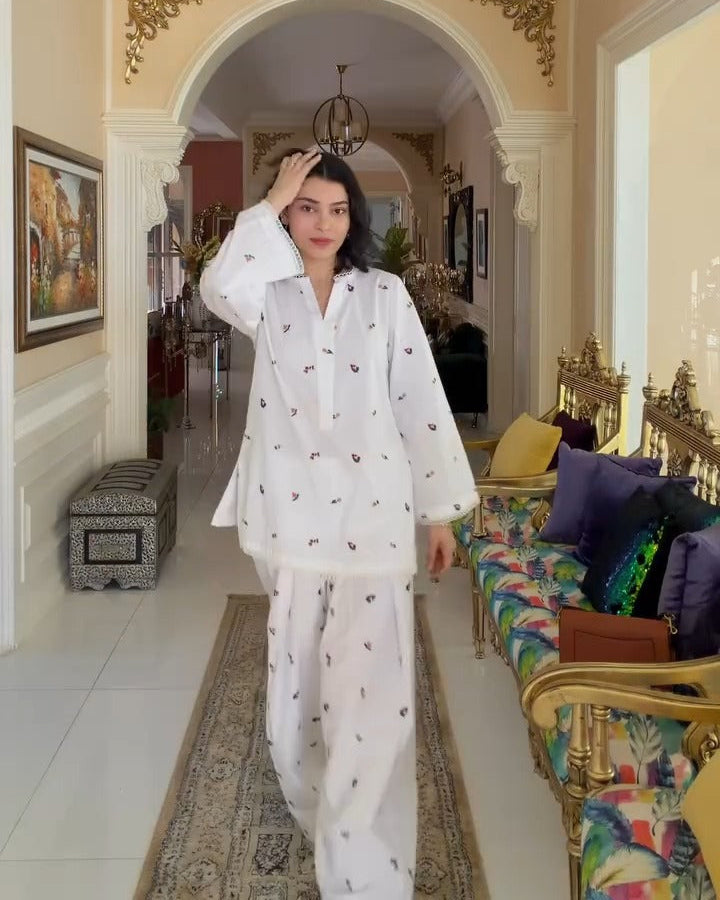 Woman in a white outfit standing in a decorated room with a chandelier and colorful sofa.