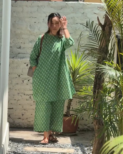 Woman in a green dress standing on a stone path with plants in the background