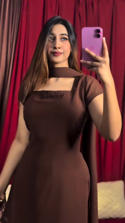 Woman in a brown dress taking a selfie with a pink phone against a red curtain background